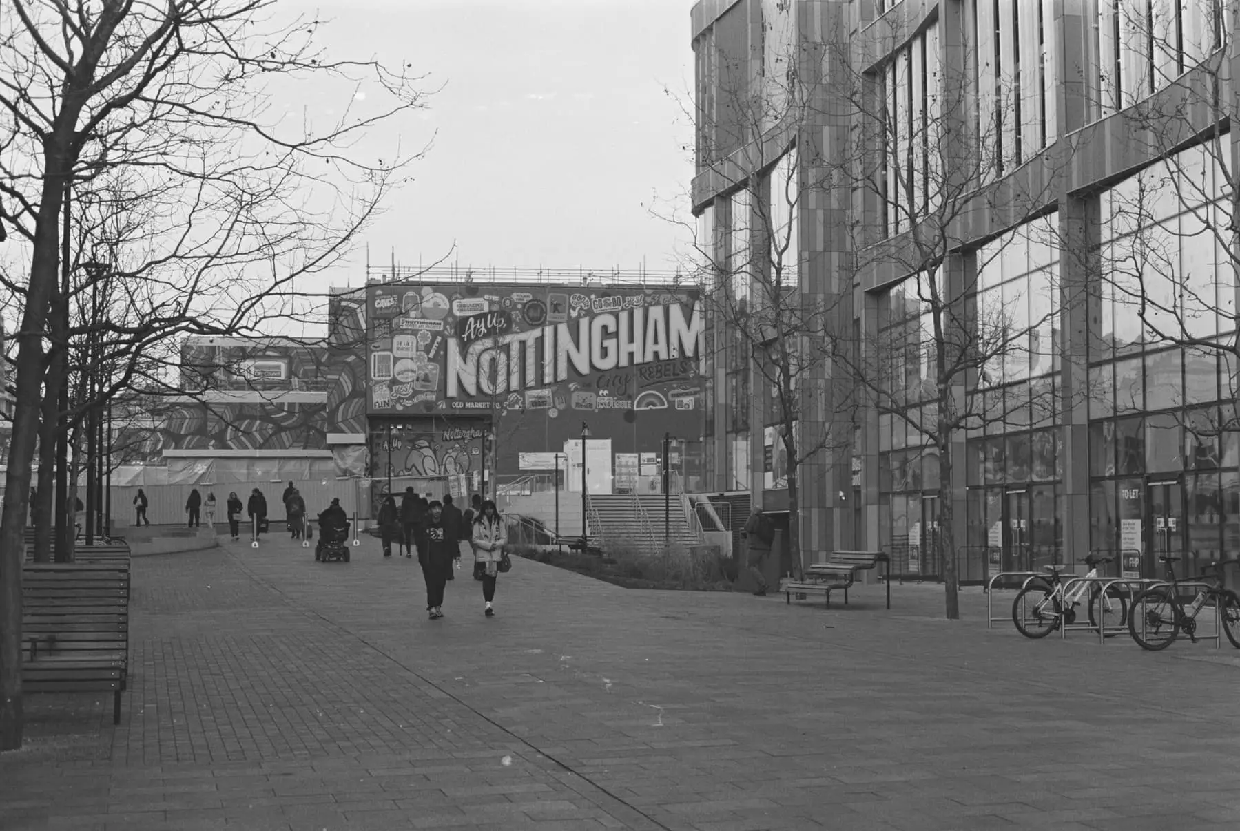 People walking along a city pavement, in black and white.